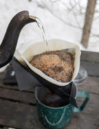 Pouring coffee from a kettle into a filter over a mug on a wooden surface.