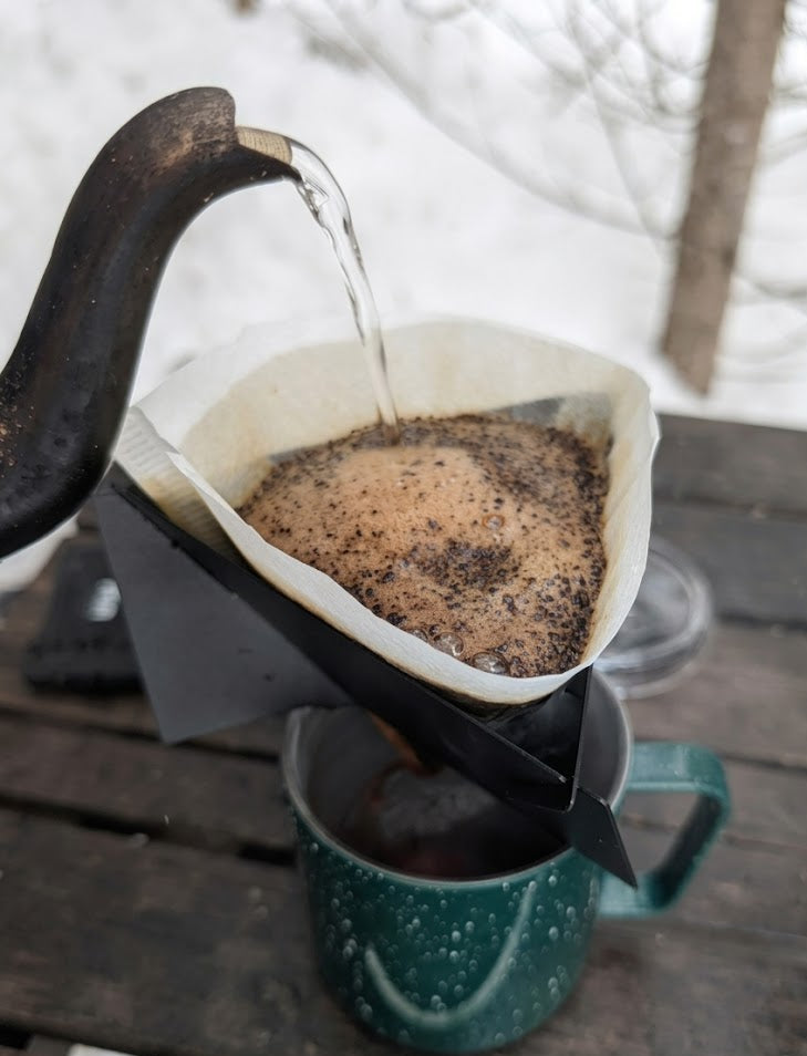 Pouring coffee from a kettle into a filter over a mug on a wooden surface.