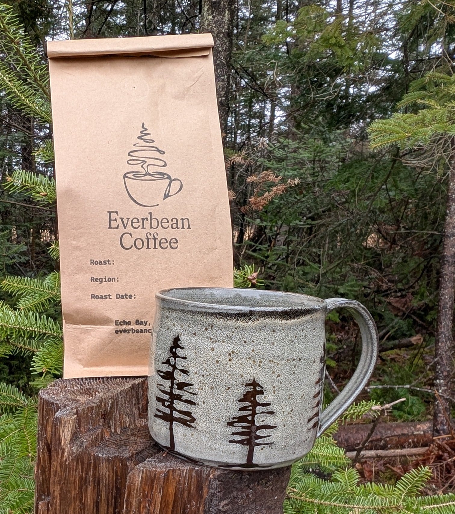 Everlean Coffee bag and ceramic mug with tree design on a wooden stump outdoors.